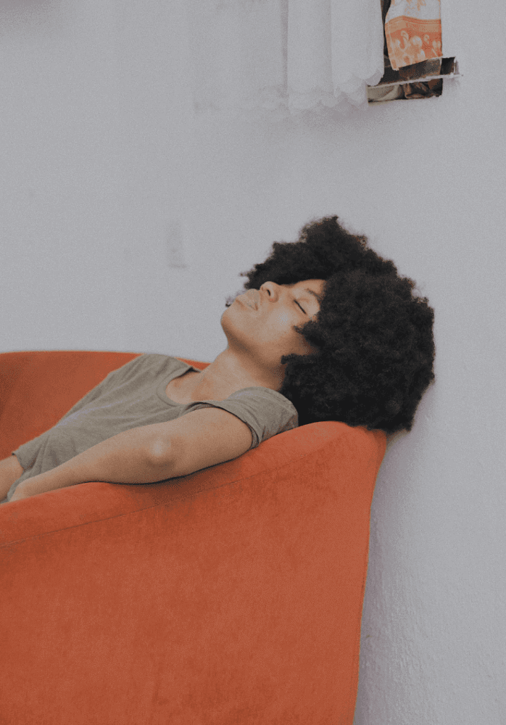 A woman with a afro sleeping against a couch showing the importance of rest days in fitness