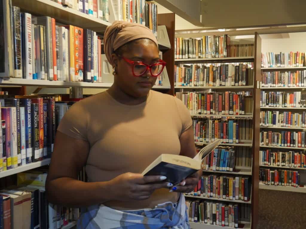 Brianna Imani reading a book a the library showing self-acceptance and loving her hobbies.