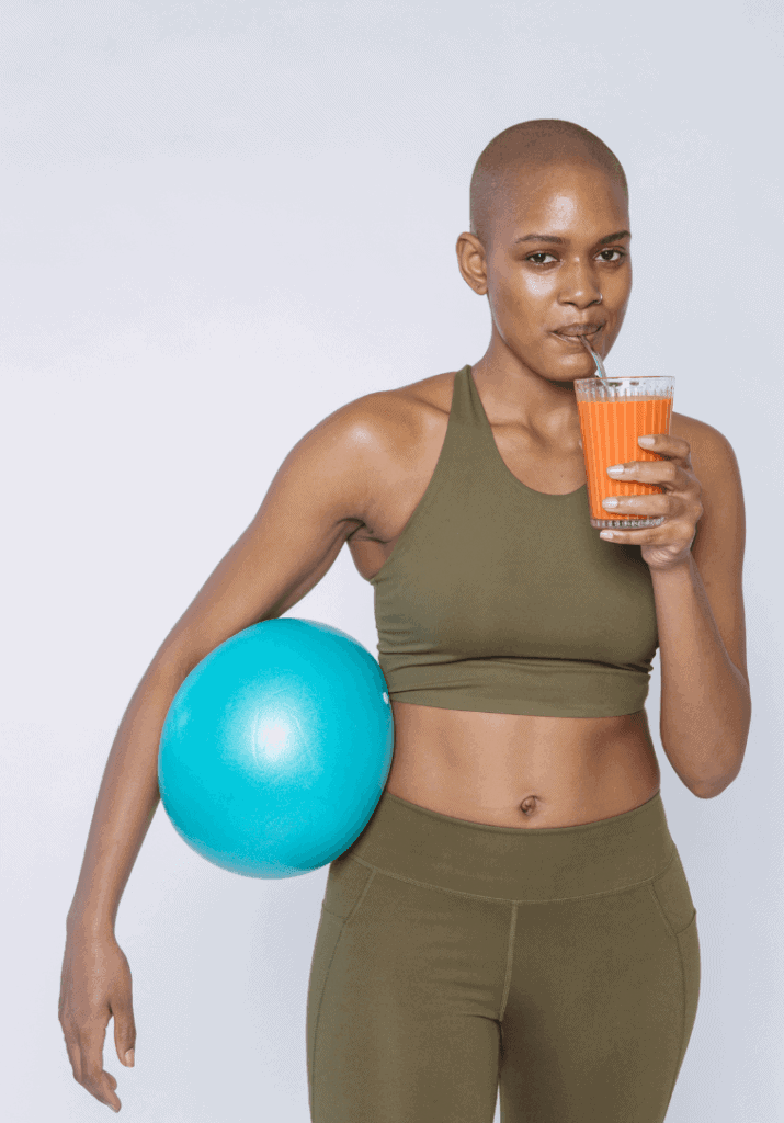 A woman is drinking an orange health drink with a fitness ball