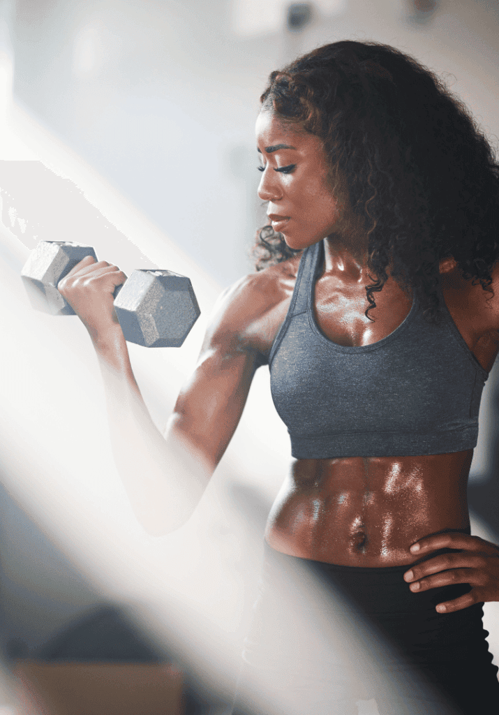 A black woman who with abs at the gym lifting a dumbbell on her realistic fitness journey.