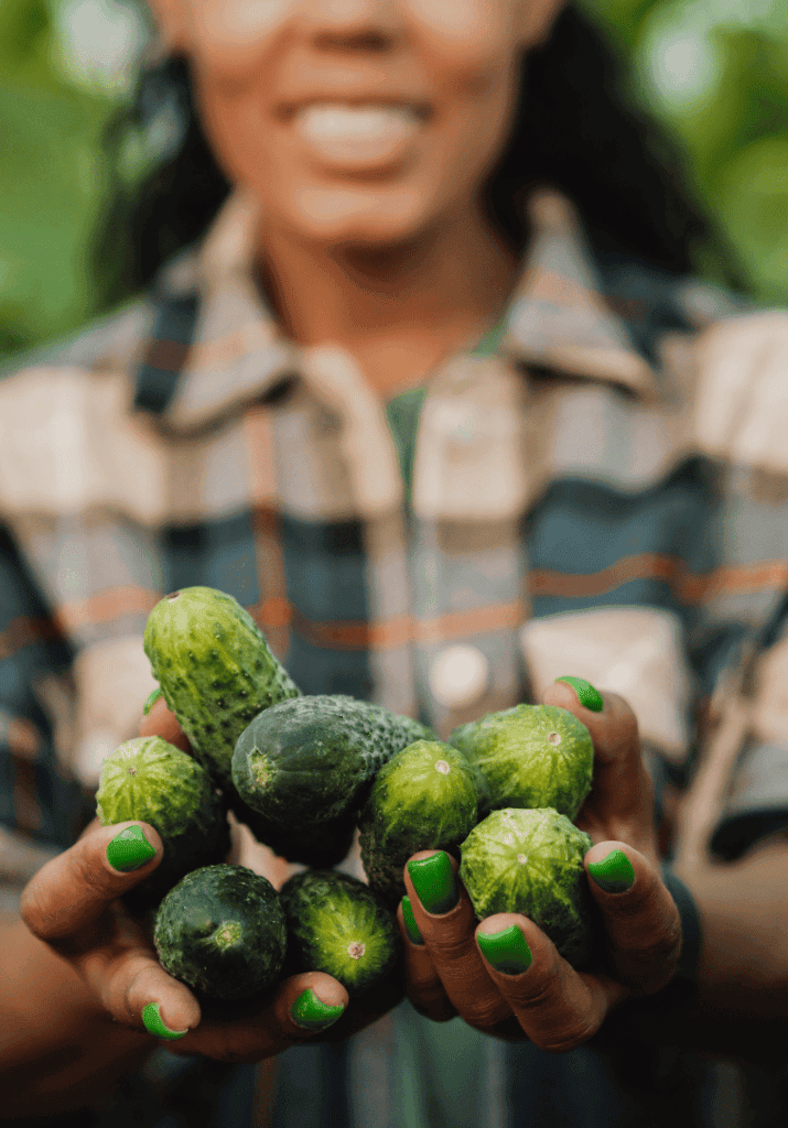 a woman holding up cumbers she's grown in her garden.