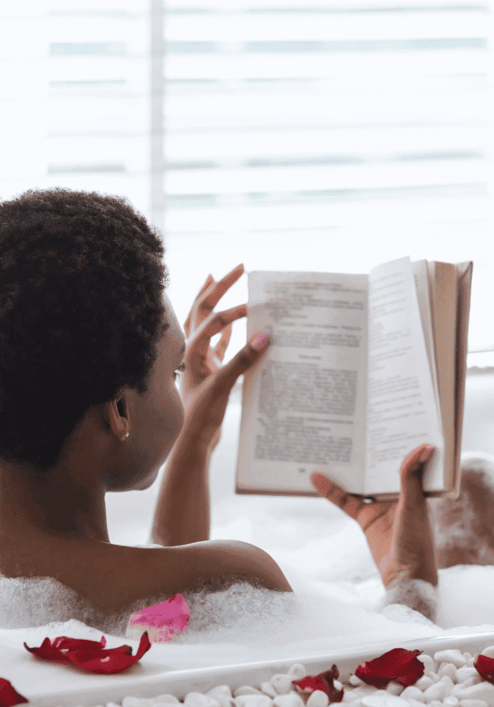 a black woman reading a book in the bath tub as a form of self-care