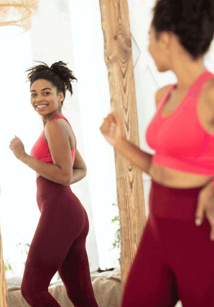 A woman smiling at her weight loss progress in the mirror