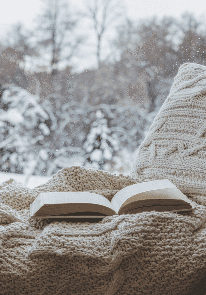 a holiday romance book on a chair next to a snowy window