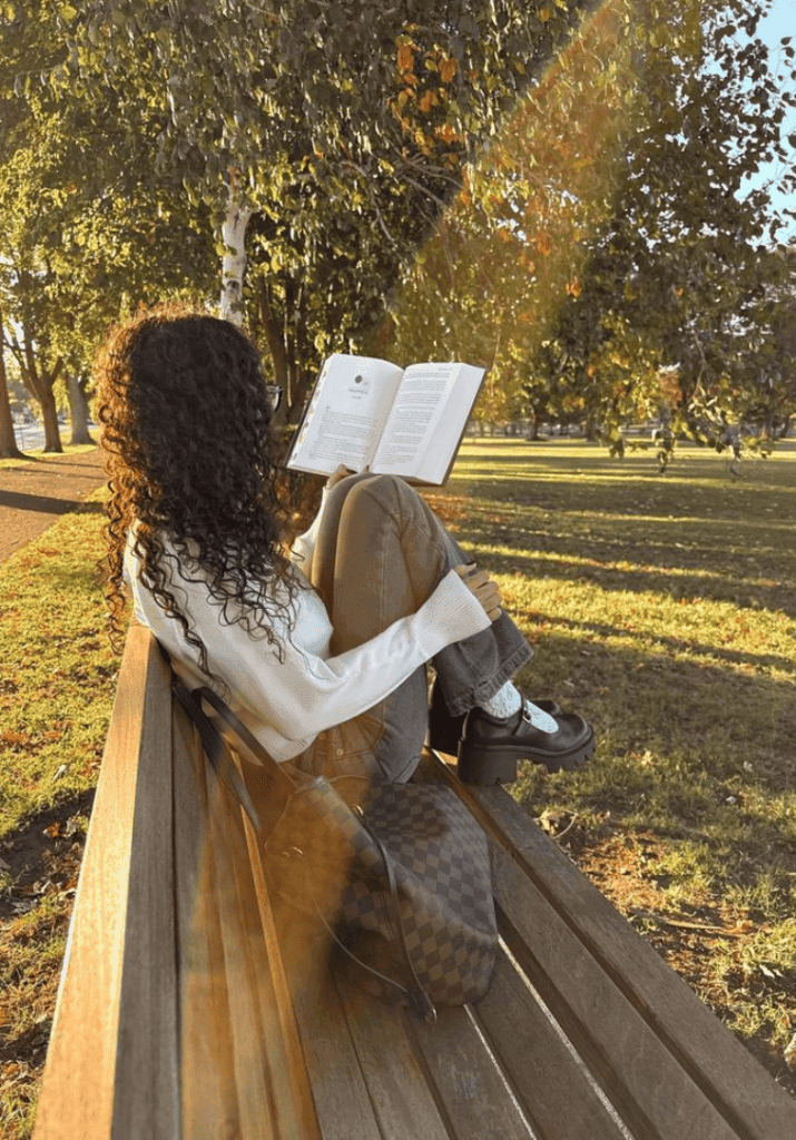 Girl sitting outdoors reading a romance novel surrounded by nature